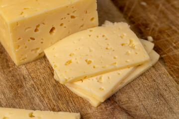 cheese with holes for cooking, pieces of sliced cheese on a cutting board, closeup