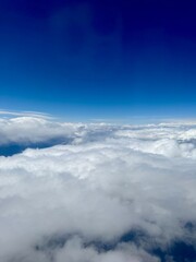Thick white clouds stretch endlessly beneath a deep blue sky, viewed from high altitude, creating a soft and peaceful aerial scene above the earth.