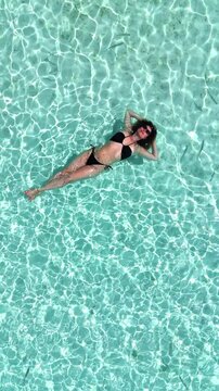 Woman floating in crystal clear turquoise water, arms stretched, enjoying relaxation on tropical island, peaceful leisure moment, travel, summer vacation, hotel promo, Maldives