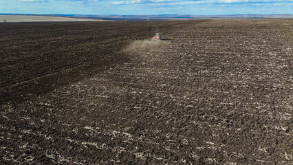 A red tractor works on a plowed field in spring, Russia farming