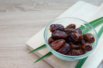 Glass Bowl of Fresh Dates with Tropical Leaves on Wooden Background