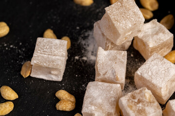 Turkish delight in powdered sugar with nuts inside, oriental sweets Turkish delight with peanuts on a black slate board, closeup