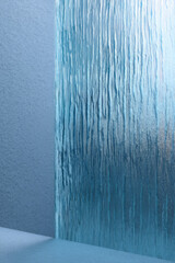 Vertical textured glass panel with streaks resembling water cascading down. Light blue hues create a calming effect. Soft shadows form on the adjacent wall surface