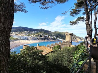 Naklejka premium Tourists enjoying panoramic view of the iconic medieval castle and the vibrant beach of tossa de mar, a popular tourist destination on the costa brava, spain, on a bright sunny day