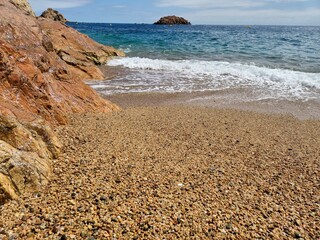 Gentle waves lapping against a pebble beach, adorned with striking red rocks and vibrant turquoise...