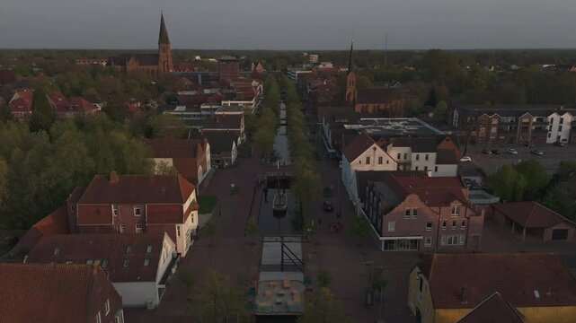 Aerial shot over Papenburg&rsquo;s Hauptkanal at sunset, with the iconic St. Antonius Church in the background and a historic ship in the canal. Red rooftops and warm evening light. Shot in 4K.