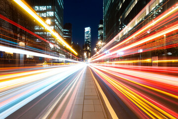 Urban nightscape showcasing dynamic light trails from vehicles on a bustling city street with modern buildings