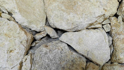 Detailed image of weathered rock masonry showing organic cracks and textures in light-colored stacked stones for construction