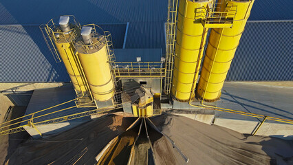 Aerial View of Industrial Yellow Silos. Top-down view of yellow industrial silos at a manufacturing facility, with conveyor systems and material piles in a factory setting. © Iryna