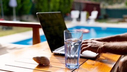 work from home concept, young man works on computer in the garden of his house with pool, writes email