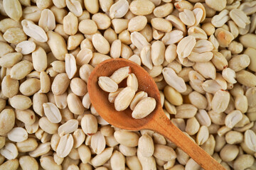 Shelled peanuts in wooden spoon on peanut background flat lay