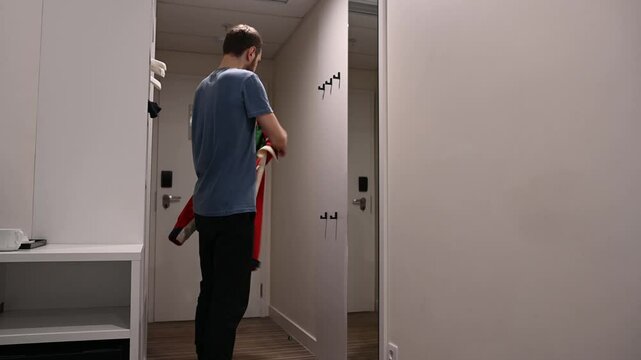The man puts on his jacket and leaves the house with the lights off.