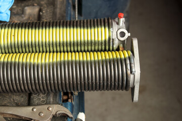 New garage door spring or coil ready to be installed. Parking gate torsion spring from overhead sectional door with yellow spray paint line. Repair work part on garage gate. Selective focus.