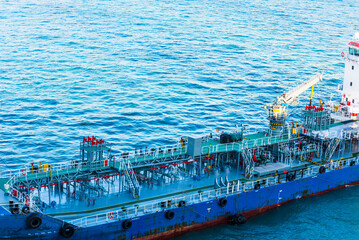 Close-up aerial view on the tanker ship, fuel bunker barge in the container terminal, she is arriving to supply large cargo ship with fuel oil. 