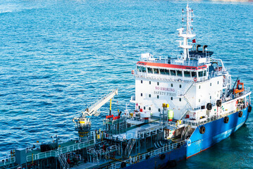 Close-up aerial view on the tanker ship, fuel bunker barge in the container terminal, she is arriving to supply large cargo ship with fuel oil. 