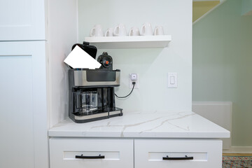 A coffee pot sits plugged in on the kitchen counter, ready to brew, while a row of coffee cups rests neatly on the shelf above.