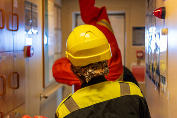 Crew members in blue coveralls and yellow helmets seen from behind during a safety drill on a...