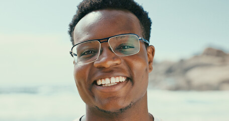 Portrait, smile and black man at beach for holiday, vacation and travel outdoor for adventure. Ocean, tourism and happy person with glasses in nature at sea for trip, relax and summer in Seychelles