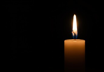 A close-up captures a candle flame dancing against a deep black backdrop, radiating warmth.