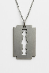 A close-up of a metal razor blade pendant hanging from a thin silver chain, with a small vent (cutout design) in the center, photographed against a clean white background