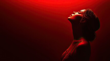 Obraz premium A woman stands in profile against a dark background, illuminated by a soft red light.