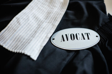 Une robe d'avocat noir posée sur une table avec dessus, une carte qui indique avocat