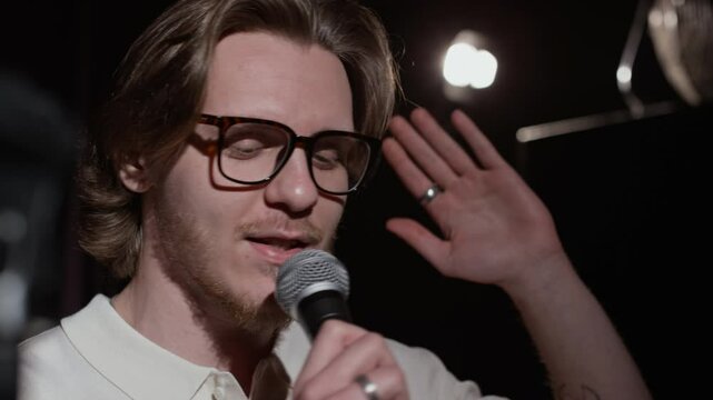 Close-up shot of bearded man in glasses telling story on stage, holding microphone during stand-up performance