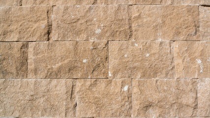 Obraz premium Close-up of a textured stone wall made of rectangular sandstone blocks. The rough surface features natural imperfections, earthy beige tones, and a rugged, organic appearance. Ideal for background.