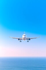 A white passenger jet descends towards a calm ocean under a vibrant blue sky
