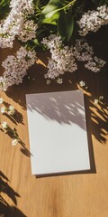 Blank greeting card mockup on wooden table with lilac and daisy flowers casting soft shadows in warm sunlight