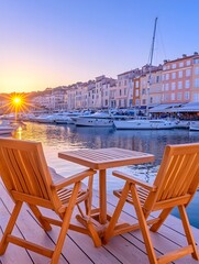 Sunset view of a harbor from a waterfront cafe with two wooden chairs and table