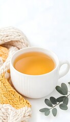 Warm beverage in a white mug, nestled beside a cozy knit scarf and eucalyptus sprigs on a bright background