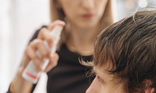 A female hairdresser cuts a teenage boy's hair in a salon setting. This image can be used for content related to hairdressing, youth culture, style, and personal care