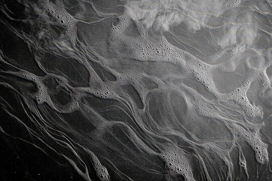 Abstract texture of dark surface with flowing patterns of white foam.
