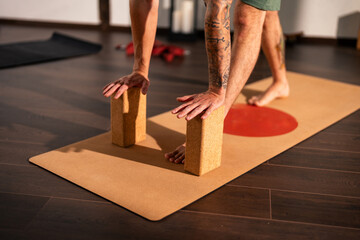 Person practicing yoga on a mat using two cork yoga blocks for support. The person is barefoot and has tattoos on their arms. The setting appears to be indoors with wooden flooring.
