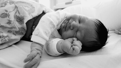 Newborn baby sleeping peacefully with a slight grimace, showing gentle hand movements in a...