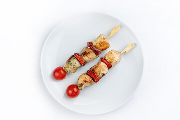 Grilled chicken kebab on skewers with tomatoes on a white plate