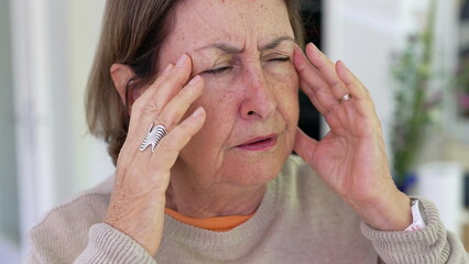Senior woman under significant stress, massaging temples with fingers, eyes closed in focus,...