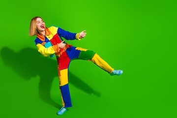 Cheerful young woman in colorful patchwork outfit against vibrant green background enjoying lively...
