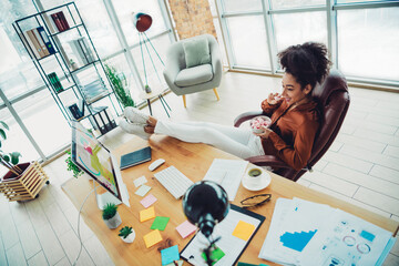Casual young businesswoman enjoying a relaxed break at her desk in a bright modern office with...