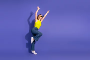 Fotobehang Young woman in vibrant outfit posing energetically against purple background showcasing youthful style and cheerful gesture © deagreez