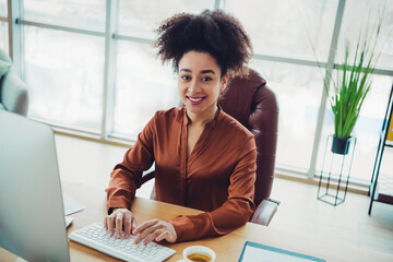 Young businesswoman with natural hair at her desk in a modern office, smiling and working on a...