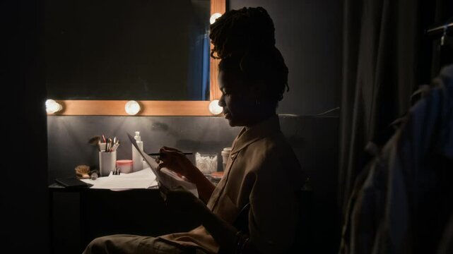 African American stand-up artist reading her performance script and making notes in dimly lit dressing room
