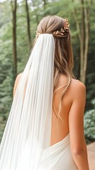 Back view of bride in flowing white dress and veil, adorned with a gold hairpiece, outdoors in a forest