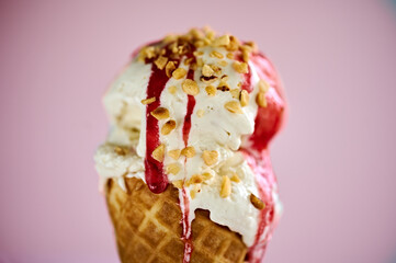 A vanilla ice-cream cone with strawberry sauce and chopped nuts toppings. Close-up.