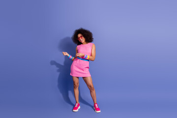 Joyful young woman in a vibrant pink dress dancing confidently against a bold purple background,...