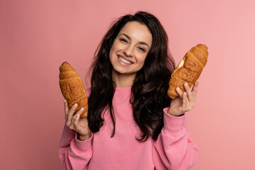 Happy cute young dark-haired woman posing for the camera with her favorite baked goods on the pink...