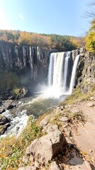Fototapeta premium Majestic waterfall cascading down rocky cliffs, surrounded by autumnal foliage A scenic view from a rocky vantage point