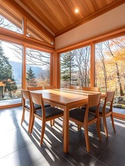 Obraz premium Sunlit dining room with large windows showcasing autumnal forest views Wooden table and chairs