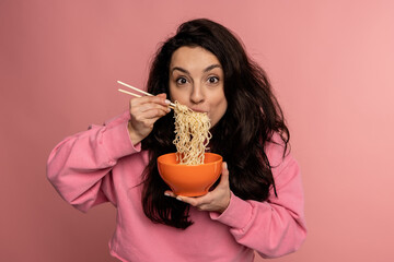 Hungry dark-haired young Caucasian woman eating pasta with an appetite during the studio photo...